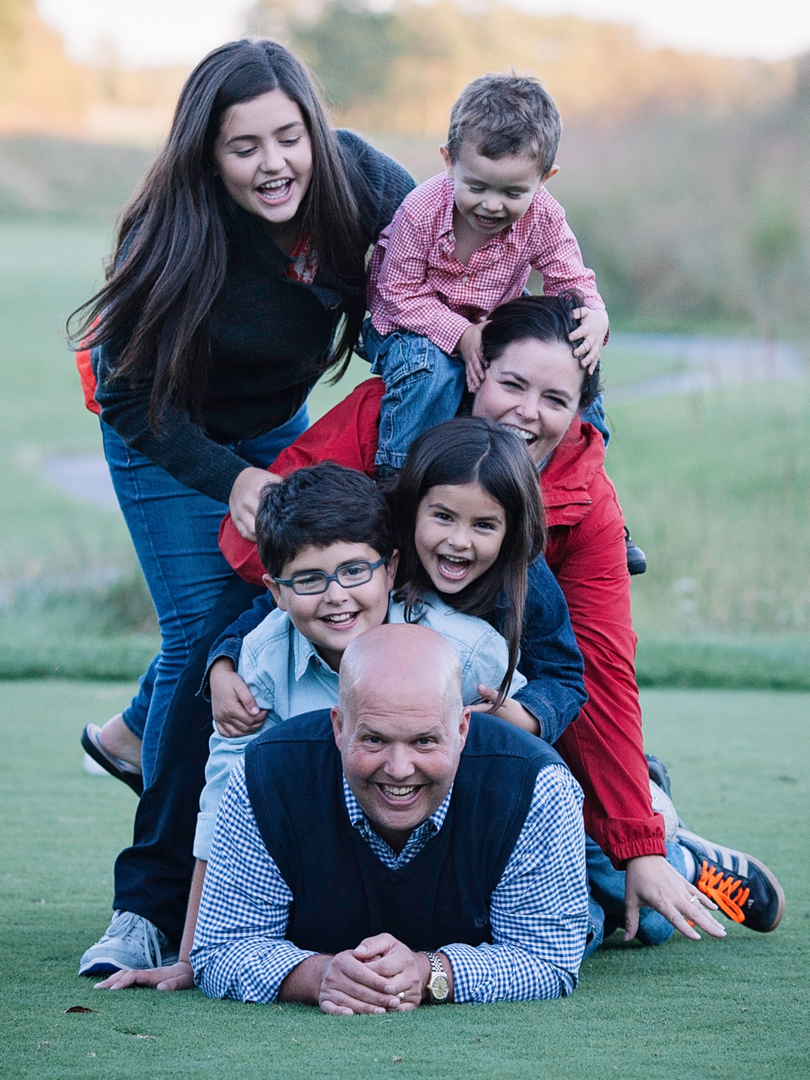 Dr. George and family in a tall pile with kids and Mrs. Bullard on top of his back, Dr. George on the bottom of the pile, all smiling at the camera